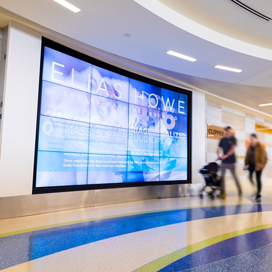 Passengers walk by large screen at Boston Logan Airport