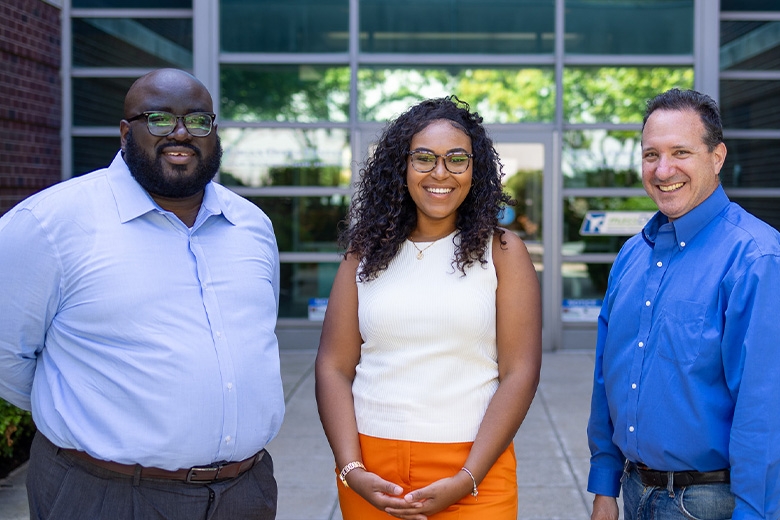 Three people in business casual attire smiling in front of office building